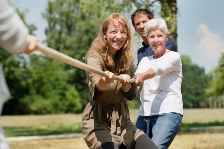 Tauziehen für ein gemeinsames Ziel Zwei Frauen und ein Mann beim Tauziehen als Symbol für gemeinsame Anstrengungen und gleiche Ziele