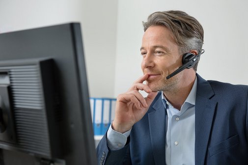 Anruf beim VdK Mann mit Headset vor einem Computerbildschirm, er telefoniert, führt nachdenklich die Finger zum Mund.
