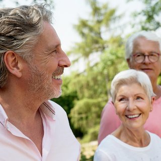 Zwei ältere Männer und eine ältere Frau sind gut gelaunt, lachen. Sie sind draußen im Grünen. 