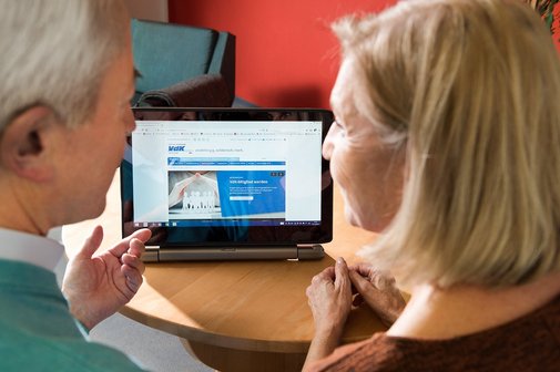 Ein älteres Paar am Computer, auf dem Bildschirm sieht man die Facebook-Seite des VdK Deutschland