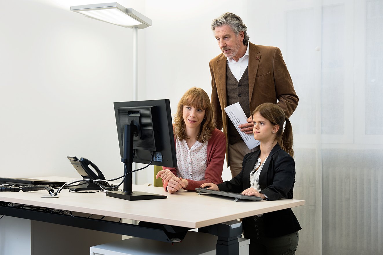 Zwei Frauen und ein Mann blicken gemeinsam auf einen Computer-Bildschirm.