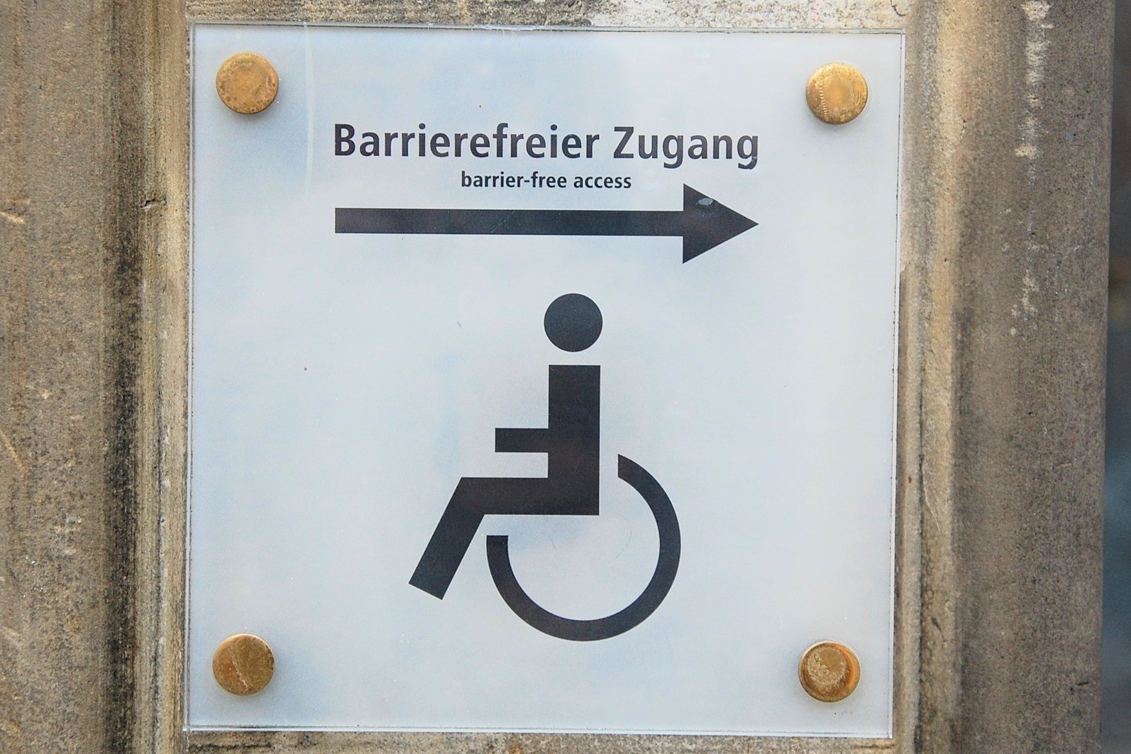 Ein Schild mit einem Rollstuhl, einem Pfeil und der Beschriftung "Barrierefreier Zugang"