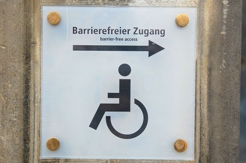 Ein Schild mit einem Rollstuhl, einem Pfeil und der Beschriftung "Barrierefreier Zugang"