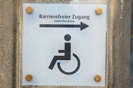 Ein Schild mit einem Rollstuhl, einem Pfeil und der Beschriftung "Barrierefreier Zugang"