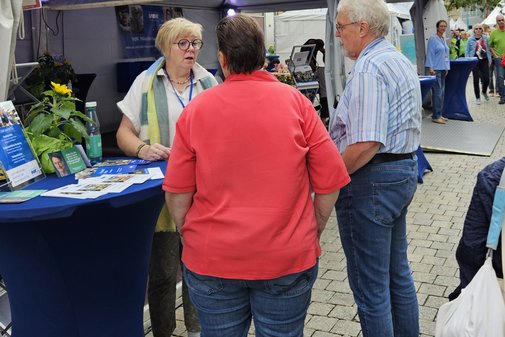 Eine Ehrenamtliche mit zwei Besuchern am Stehtisch im Gespräch