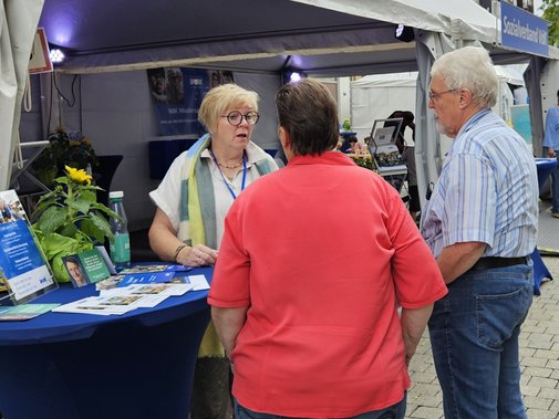 Eine Ehrenamtliche mit zwei Besuchern am Stehtisch im Gespräch