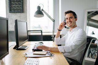 Ein junger Mann im weißen Hemd am Schreibtisch mit einem Computer