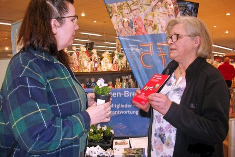 Eine Ehrenamtliche &uuml;berreicht einer Besucherin eine Blume und einen Flyer.
