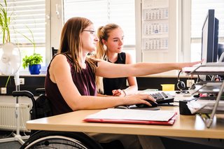 Zwei Frauen, davon eine im Rollstuhl, arbeiten gemeinsam am Computer