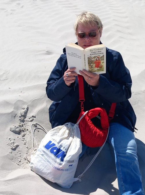 Bärbel auf dem Sand mit Buch und VdK-Rucksack
