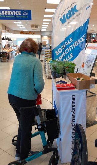 Eine Frau am blau-weißen VdK-Infostand, im Hintergrund ist der Verbrauchermarkt zu sehen