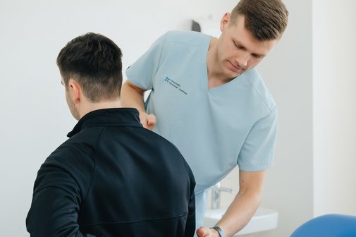 Physiotherapeut unterst&uuml;tzt einen Patienten mit R&uuml;ckenschmerzen in einer Klinik.