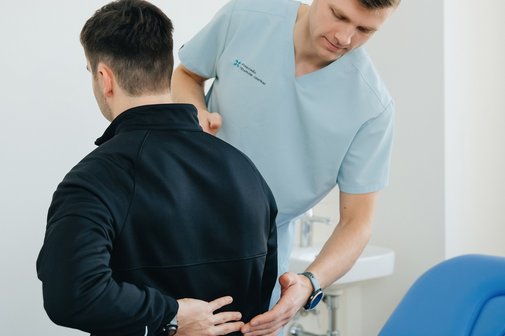 Physiotherapeut unterstützt einen Patienten mit Rückenschmerzen in einer Klinik.