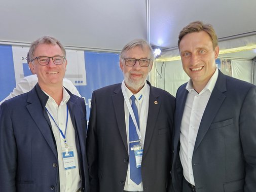 Die drei Männer im Anzug im blau-weißen Infostand