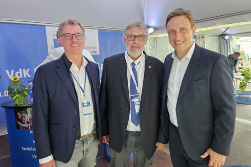 Die drei Männer im Anzug im blau-weißen Infostand