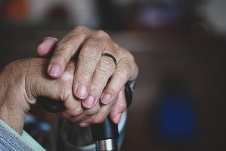 Zwei gepflegte ältere Frauenhände, die sich auf einen Gehstock stützen