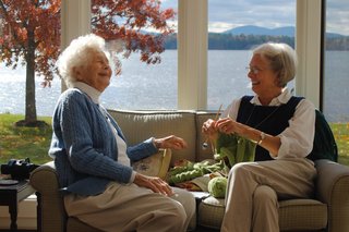 Zwei fröhliche ältere Frauen auf einem Sofa im Gespräch