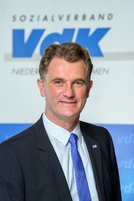 Holger Grond lächelnd vor dem VdK-Logo in Blau