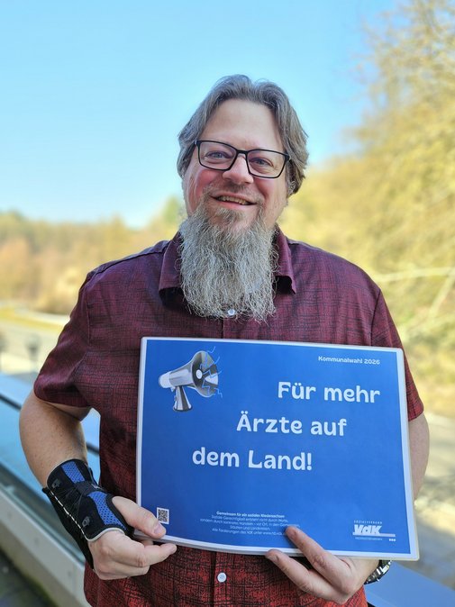 Thorsten Baumgarten h&auml;lt l&auml;chelnd ein Schild mit den Forderungen hoch 