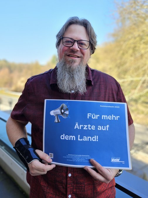 Thorsten Baumgarten h&auml;lt l&auml;chelnd ein Schild mit den Forderungen hoch 