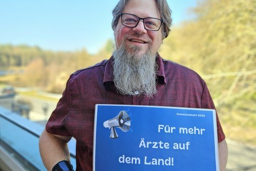 Thorsten Baumgarten h&auml;lt l&auml;chelnd ein Schild mit den Forderungen hoch 