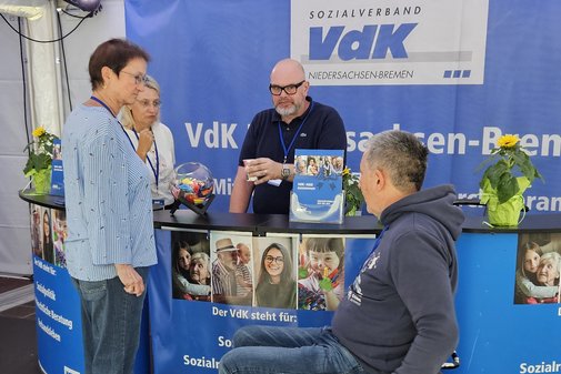 Vier VdKler, davon einer im Rollstuhl, im Gespräch am blauen Infotresen