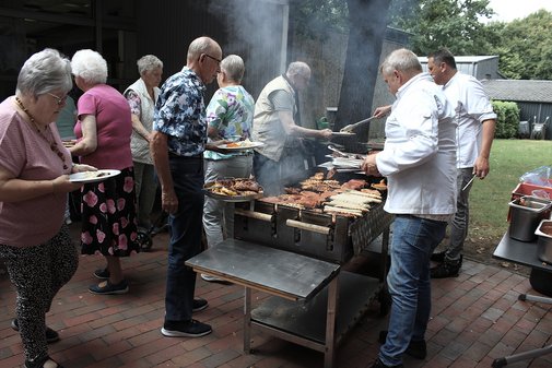 Männer und Frauen am Grillbuffet und zwei Männer am Grill