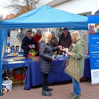 VdK-Ehrenamtliche zusammen mit Interessierten am blauen VdK-Infostand in Uelzen im März 2024