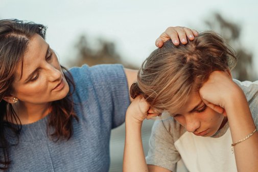 Eine Frau wuschelt einem Jungen zur Aufmunterung durch die Haare