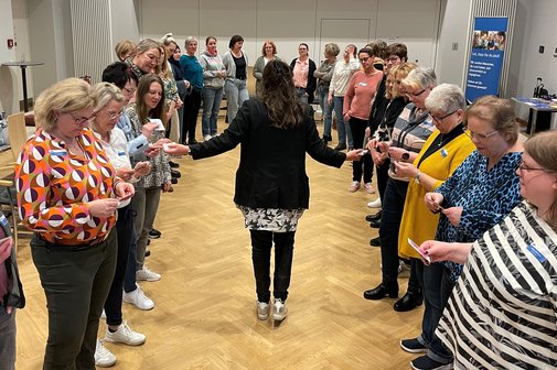 Rubina Ordemann verteilt Karten an die Assistentinnen, die im Halbkreis stehen