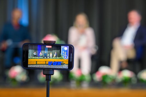 Ein Smartphone auf einem Stativ, das eine Talkrunde mit VdK-Logo zeigt