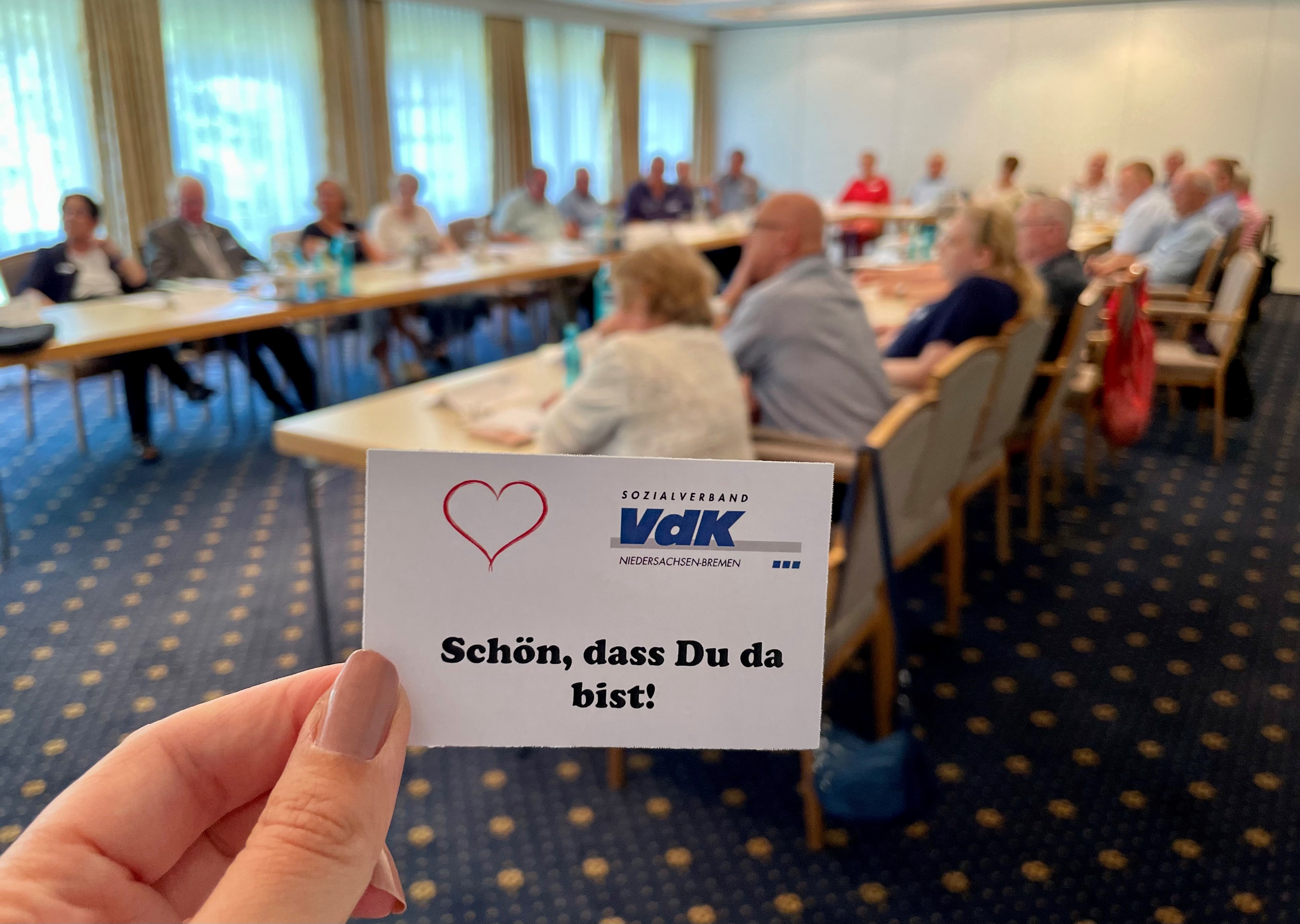 Eine Karte mit "Sch&ouml;n, dass du da bist". Im Hintergrund VdKler bei einem Treffen an Tischen