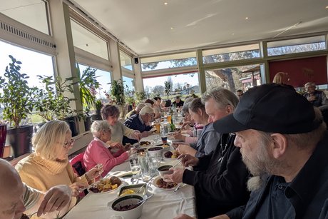 Mehrere Personen sitzen an einer langen Tischreihe und essen gemeinsam Rouladen.