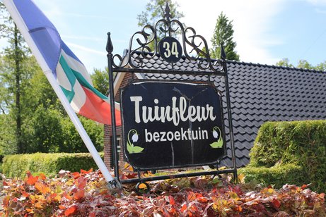 Schild mit der Bezeichnung Tuinfleur bezoektuin vor einem Hausdach.