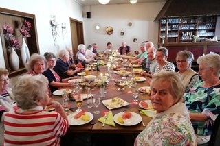 Menschen sitzen in einer Gaststätte an einem reichlich gedackten Tisch