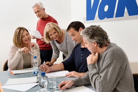 Verschiedene Menschen sitzen an einem Tisch, offenbar in einer Arbeitssitzung, an der Wand hinter ihnen ist ein gro&szlig;es VdK-Logo.
