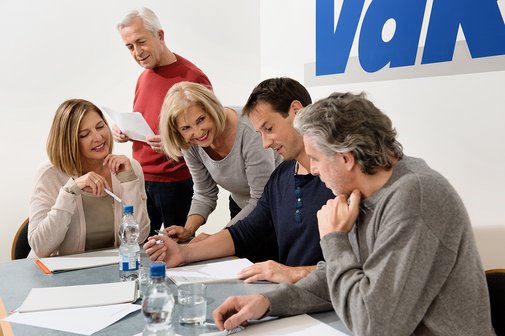 Verschiedene Menschen sitzen an einem Tisch, offenbar in einer Arbeitssitzung, an der Wand hinter ihnen ist ein gro&szlig;es VdK-Logo.