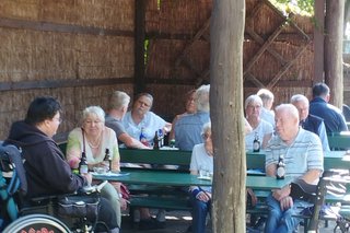 Das Bild zeigt eine Gruppe von Menschen, die sich an einem Tisch unter einem Unterstand sitzen. Der Alte Fahnster Krug ist auch für Menschen mit Mobilitätseinschränkungen zugänglich.