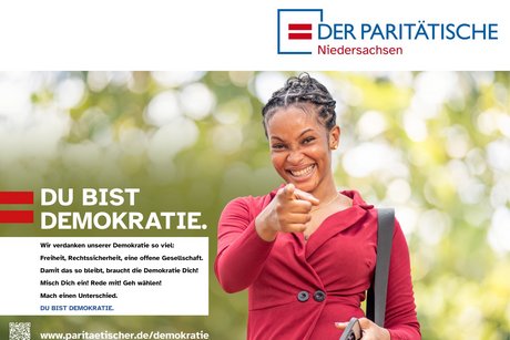 Kampagnenmotiv „Du bist Demokratie“ Das Bild zeigt eine junge Frau, welche ein rotes Langarm-Shirt trägt und auf die betrachtende Person zeigt. Links daneben steht der Slogan „Du bist Demokratie“.