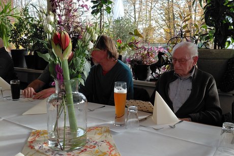 Das Foto zeigt Gäste an einem Tisch. Ein Gast sitzt vor einen gefüllten Weizenbierglas. Auf dem Tisch steht herbstliche Dekoration.