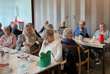 Zuh&ouml;rerinnen und Zuh&ouml;rer sitzen an Tischen
