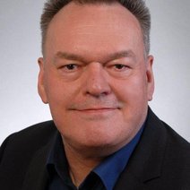 Ein l&auml;chelnder Mann, mit dunkel blauem Hemd und anthrazitfarbenen Sacko