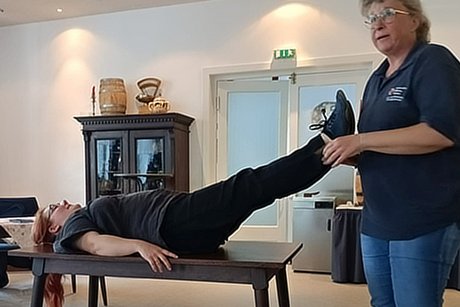 Frau Christiane Gentzmann vom DRK Kreisverband Celle e.V. zeigt, was zu tun ist, wenn jemandem der Kreislauf zusammenbricht. Frau Wolski liegt auf einem Tisch, Frau Gentzmann h&auml;llt ihre Beine in die H&ouml;he.