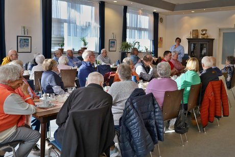 Die Teilnehmerinnen und Teilnehmer unseres monatlichen Treffens sitzen an Tischen und h&ouml;ren dem Vortrag von Frau Julia Dittel zu.