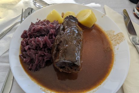 Das Bild zeigt einen wei&szlig;en Porzellanteller mit einer Roulade, Sauce, Salzkartoffeln und Rotkraut.