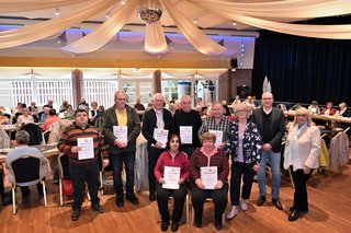 Die geehrten Mitglieder stehen mit ihren Urkunden vor den Mitgliedern im edel geschmückten Saal