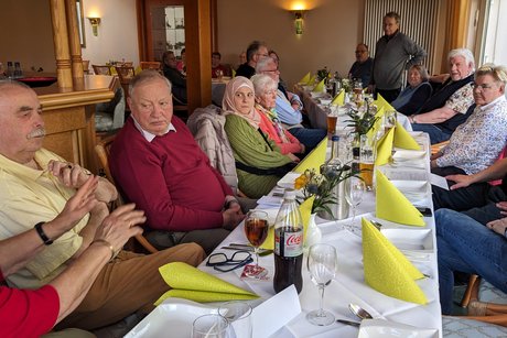 Blick in den Gastraum von Seekamps Centralhallen. Es sind ca. 15 der anwesenden Personen zu sehen; der Vorsitzende stehend bei dem Bericht.