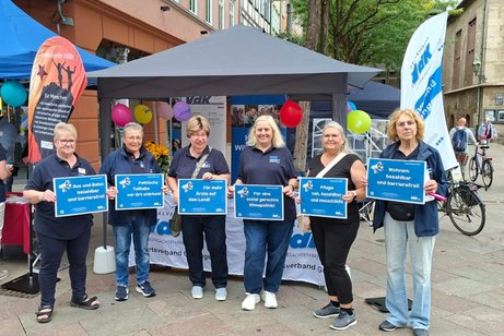 sechs Frauen stehen vor dem Stand des VdK und halten Plakate mit den Vorderungen vom VdK