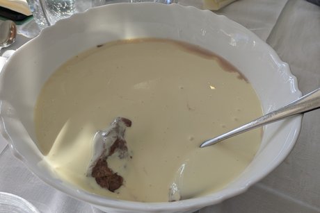 Das Bild zeigt eine wei&szlig;e Porzellansch&uuml;ssel, gef&uuml;llt mit Schokoladen-Pudding. Der Pudding ist mit Vanille-Sauce bedeckt.