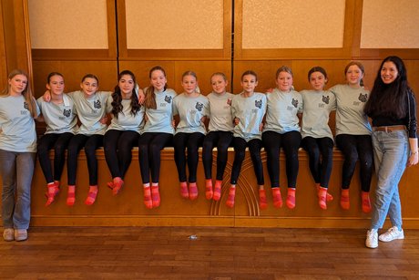Die 10 Cheerleader der Wilhelm-Olbers-Oberschule sitzen auf der Bühne des Saals und werden umrahmt von den beiden Betreuerinnen.